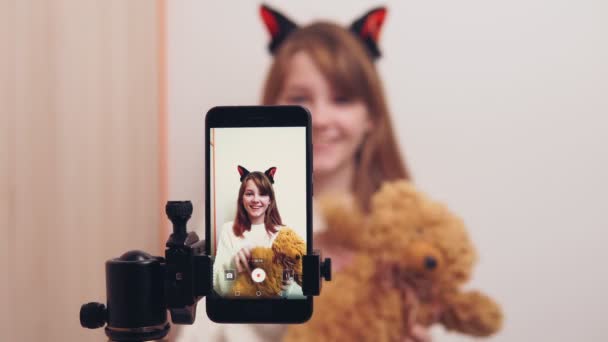 Oyuncak ayıyla mutlu bir blog yazarı sosyal ağlarda video blogu için akıllı telefon kamerası kullanıyor, aboneleri karşılıyor. — Stok video