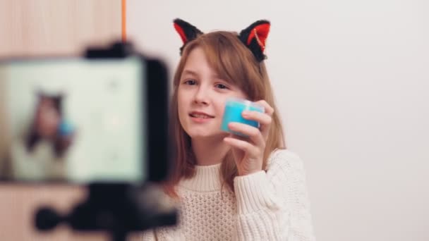 Leuk gelukkig meisje gebruikt een smartphone voor een video blog op sociale netwerken. Een meisje blogger shows en praat op de telefoon camera over een speelgoed slijm. — Stockvideo