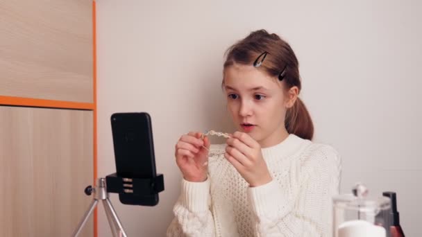 Élégant jeune fille blogueur montre ses bijoux aux abonnés. Ça t'apprend à être élégant. Enregistre une vidéo pour un blog sur les réseaux sociaux à l'aide d'une caméra smartphone sur un trépied . — Video