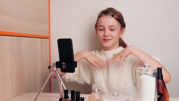 Linda chica joven maquillaje blogger muestra su nuevo lápiz labial. graba vídeo para un blog en las redes sociales usando una cámara de teléfono inteligente en un trípode . — Vídeos de Stock