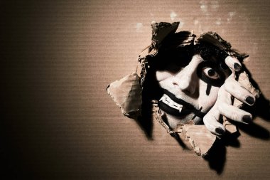 Korkunç bir vampir palyaço pençeleriyle kartondan parçalar ve kameraya bakar. Sol tarafında boşluk olan Cadılar Bayramı teması.