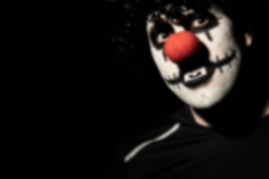 Siyah peruk ve makyajlı korkunç bir palyaçonun bulanık portresi. Kırmızı burunlu, tüyler ürpertici bir palyaço kostümü giymiş bir adam..