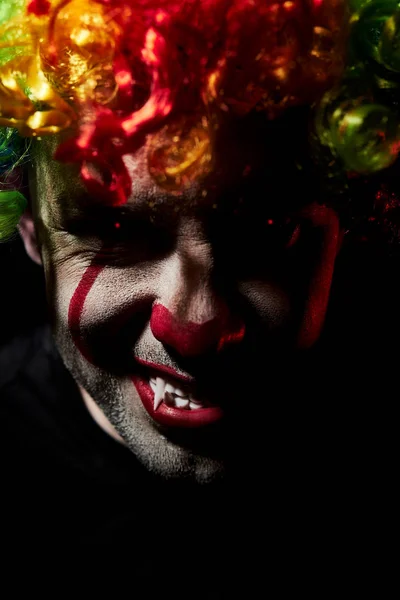 Naštvaný strašidelný klaun s vyceněnými tesáky. Detailní portrét v barevné paruce s děsivě červenýma očima — Stock fotografie