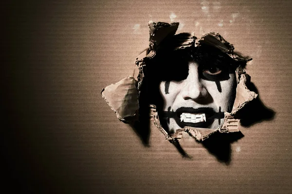Жахливий жахливий вампірський клоун дивиться через рваний картон. Тема Хеллоуїна з порожнім простором ліворуч . — стокове фото