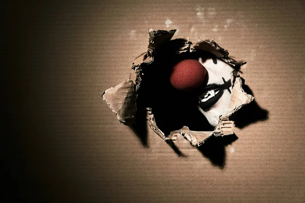 Жахливий вампірський клоун з червоним носом показує свої ікла через рваний картон. Тема Хеллоуїна з порожнім простором ліворуч . — стокове фото