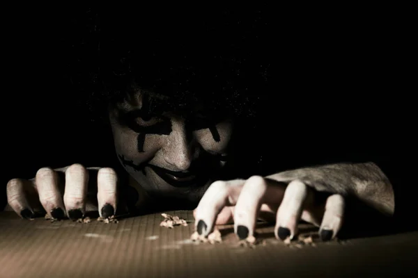 Ein gruseliger Clown guckt aus dem Keller und kratzt mit seinen Krallen den Boden. — Stockfoto