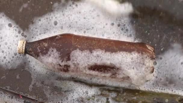 Plastic contamination of the aquatic environment. Close-up of a plastic bottle swinging on the waves off the coast of a reservoir. Top view. — Stock Video