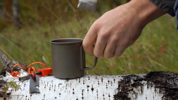 Primer plano de vídeo de un turista haciendo té. Taza de titanio en un árbol caído . — Vídeo de stock