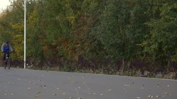 Um ciclista monta uma bicicleta em um caminho em um parque. Um jovem com roupas de ciclismo monta no outono . — Vídeo de Stock