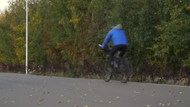 Seorang pengendara sepeda mengendarai sepeda di jalan di taman. Seorang pria muda bersepeda naik pakaian di musim gugur . — Stok Video