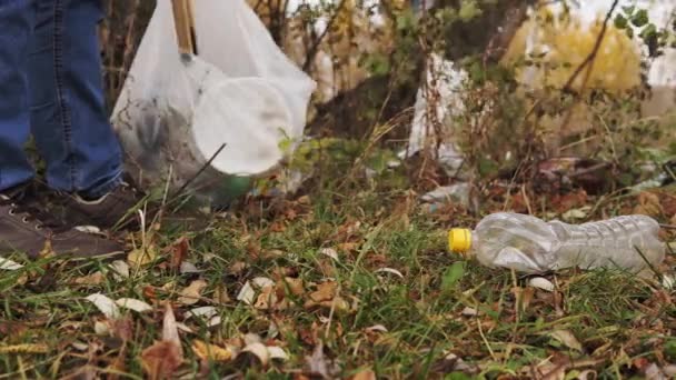 Ecological concept, collection of plastic trash on the nature. Responsible male volunteer collects garbage into a bag with wooden tongs, close-up. — Stock Video