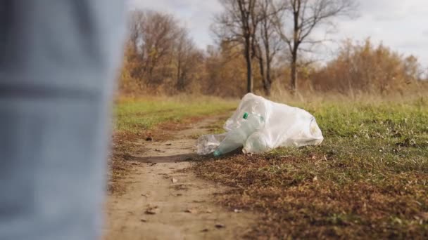 O homem polui o ambiente com plástico. Jovem inculta na natureza chuta um saco de lixo . — Vídeo de Stock