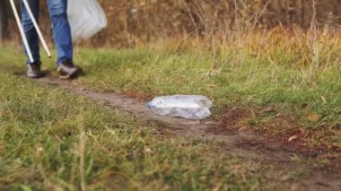Ekolojik kavram, plastiği durdur. Yakın plan, bilinci açık bir gönüllü tahta maşayla plastik bir şişeyi alıp bir torbaya koyuyor..