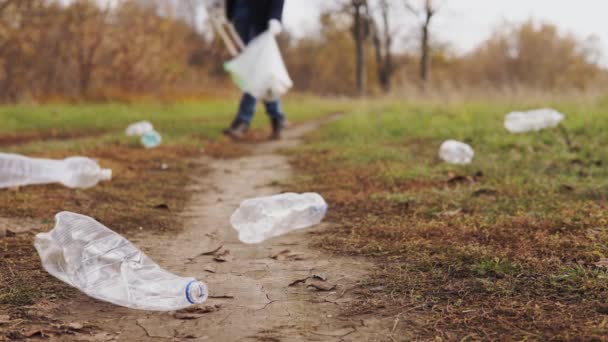 Ekologický koncept zastavit plast. Detailní záběr, zodpovědný muž dobrovolník v džínách, sbírá plastové láhve do biologicky rozložitelné tašky pomocí dřevěných kleští. — Stock video