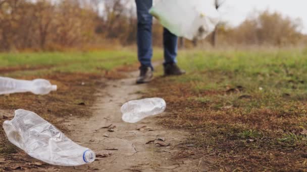 Ekologický koncept zastavit plast. Detailní záběr, zodpovědný muž dobrovolník v džínách, sbírá plastové láhve do biologicky rozložitelné tašky pomocí dřevěných kleští. — Stock video