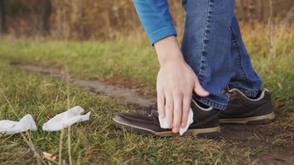 Concetto di uomo inquinamento natura. Un primo piano di un uomo irresponsabile in jeans si pulisce le scarpe con salviettine bagnate e lo getta sull'erba. . — Video Stock