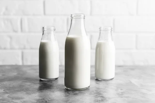 Three glass reusable bottles of milk in the kitchen with marble countertops and a white brick wall.