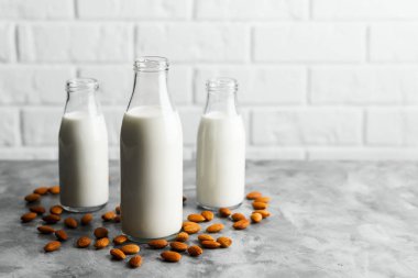 Mermer tezgahta badem sütü ve badem fıstıklı üç bardak yeniden kullanılabilir şişe, beyaz tuğlalı bir mutfak..