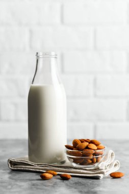 Mermer tezgahta badem sütü ve bademle yeniden kullanılabilir cam şişe, beyaz tuğlalı bir mutfak..