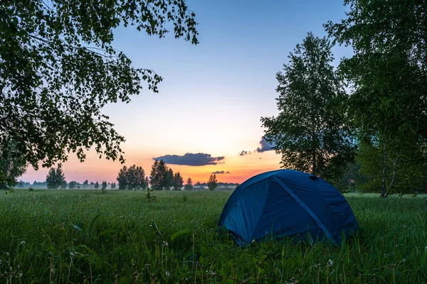 A blue tent located in a clearing in the forest. Camping tent on the background of dawn. — Stock Photo, Image