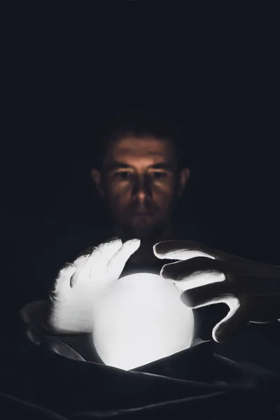 Sessão espiritual prevendo o futuro. Um homem clarividente segura as mãos sobre uma bola de cristal luminosa . — Fotografia de Stock