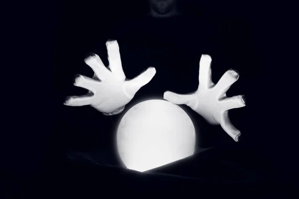 Sesión espiritual prediciendo el futuro. Manos abiertas con guantes blancos sobre una bola de cristal luminosa . — Foto de Stock