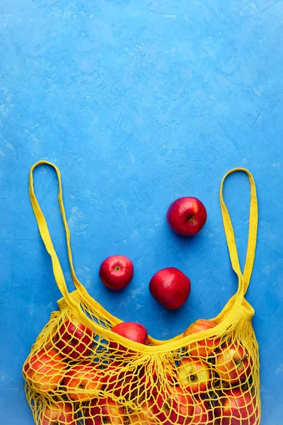 Yellow string bag with red apples on blue concrete. — Stock Photo, Image
