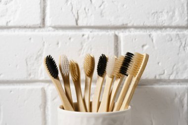 Close up of several biodegradable bamboo toothbrushes in a white glass on a brick wall background.