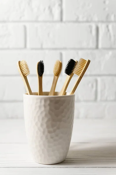 White ceramic glass with biodegradable bamboo toothbrushes on a brick wall background. Zero waste concept. — Stock Fotó
