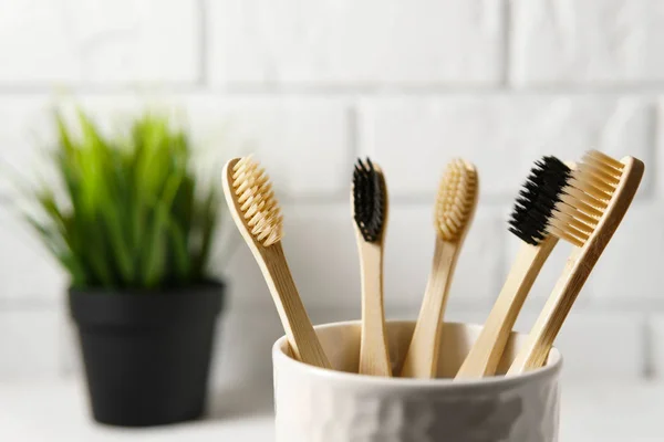 Close up of several biodegradable bamboo toothbrushes in a white glass on a brick wall background. — Stock Photo, Image