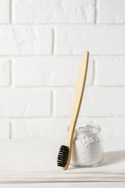 Bamboo toothbrush with a white towel and tooth powder in a bowl on a background of a light brick wall. — Stock Photo, Image