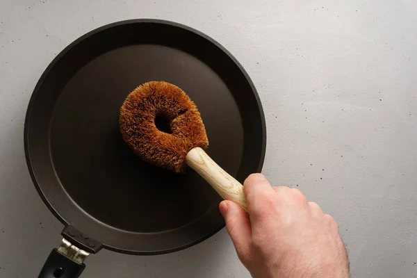 The male hand holds a brush made of coconut with a bamboo handle over the pan. — Stock Fotó