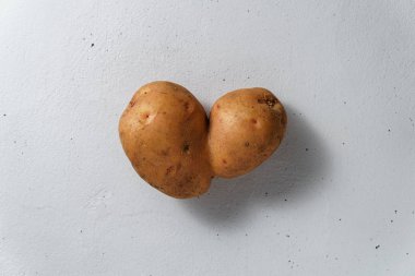 An ugly potato in the shape of a heart on a light concrete background.
