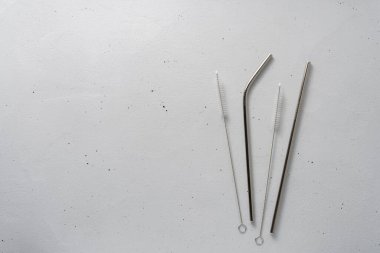 Açık gri arka planda iki metal pipet ve temizlik fırçası..