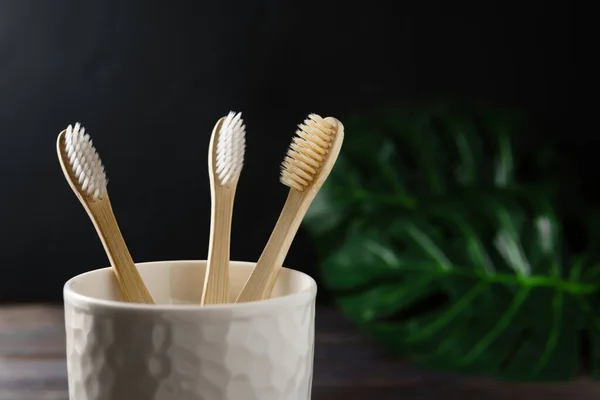 Nahaufnahme eines weißen Keramikglases mit drei biologisch abbaubaren Bambus-Zahnbürsten auf dunklem Hintergrund. — Stockfoto