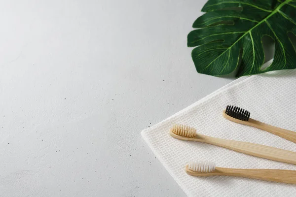 Três escovas de dentes de bambu com toalha branca em uma mesa de concreto cinza . — Fotografia de Stock