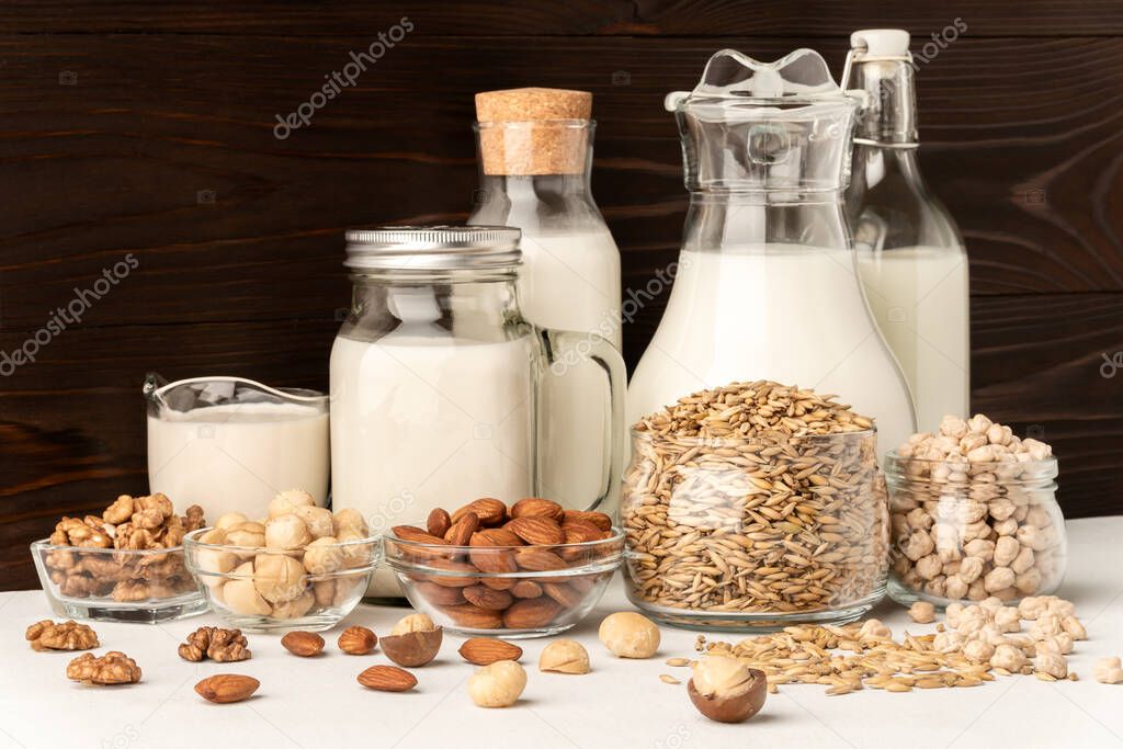 Milk from macadamia, chickpeas, oats, walnuts and almonds on a brown wooden background.