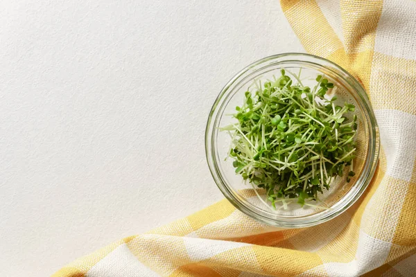 Brotes de rúcula de micro verdes frescos en un recipiente de vidrio y una servilleta de algodón sobre un fondo de hormigón gris claro . —  Fotos de Stock