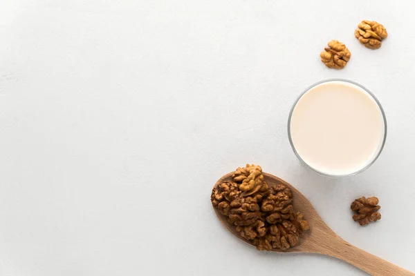 Walnut milk in a glass and a wooden spoon with nuts on a light gray concrete background. — Stock fotografie