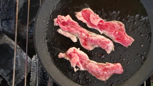 Gros plan de trois tranches de bacon frites dans une poêle dans un gril . — Video