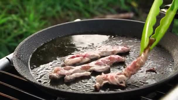 Cooking bacon in a pan over charcoal during a picnic in nature. — 비디오