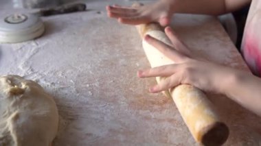 Küçük beyaz kız hamuru ahşap bir oklava kullanarak yuvarlıyor..