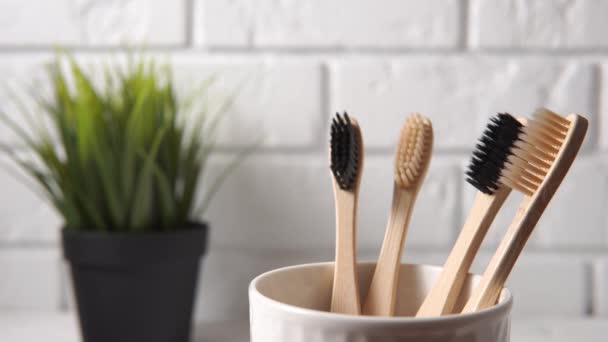 Una mano masculina pone un cepillo de dientes de bambú en una taza blanca . — Vídeos de Stock