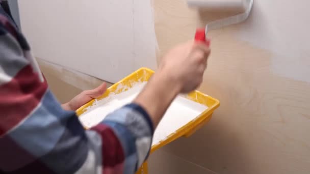 A young man in a shirt paints a white wooden surface at home. — Stock Video