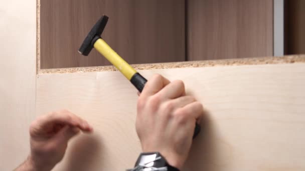 Een jonge kerel in een shirt hamert nagels in multiplex met behulp van een hamer. — Stockvideo