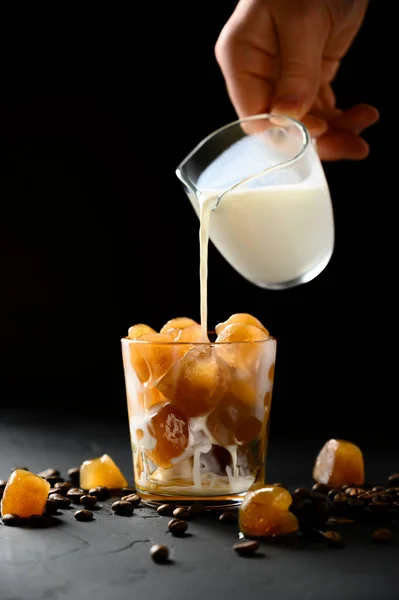 Mjölk hälls i ett glas med is från kaffe. Man häller grädde i iskaffe. — Stockfoto