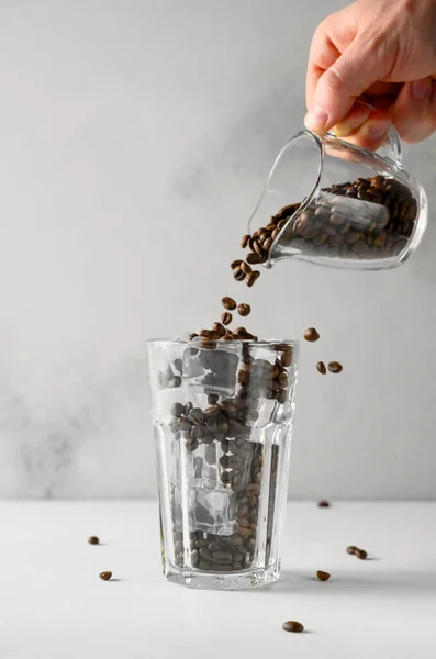 Iced konsep kopi. Sebuah tangan laki-laki menuangkan biji kopi ke gelas tinggi dengan es. — Stok Foto