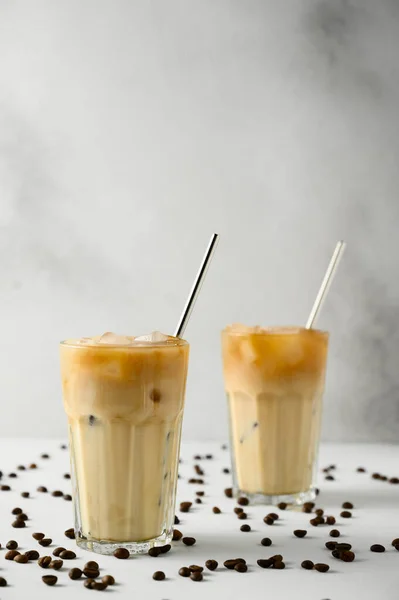 Two glasses with iced coffee and scattered grains on a light concrete surface.