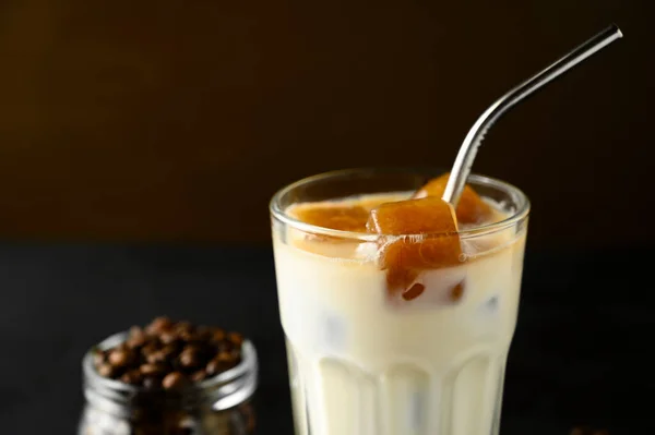 Szklanka z mlekiem i kostkami lodu z kawy. Mrożona kawa z metalową rurką na brązowym tle. — Zdjęcie stockowe