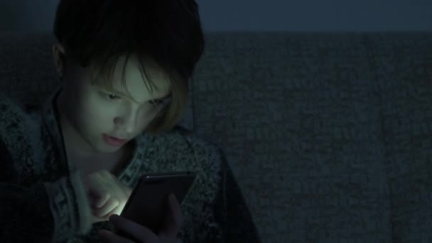 Adolescente chica utiliza un teléfono inteligente en un cuarto oscuro . — Vídeos de Stock
